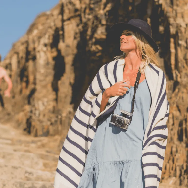 Woman walking to the beach wearing a striped top and a camera around her neck
