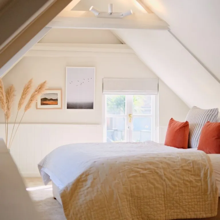 Master bedroom with low ceilings, art prints, pampas grass and orange cushions.