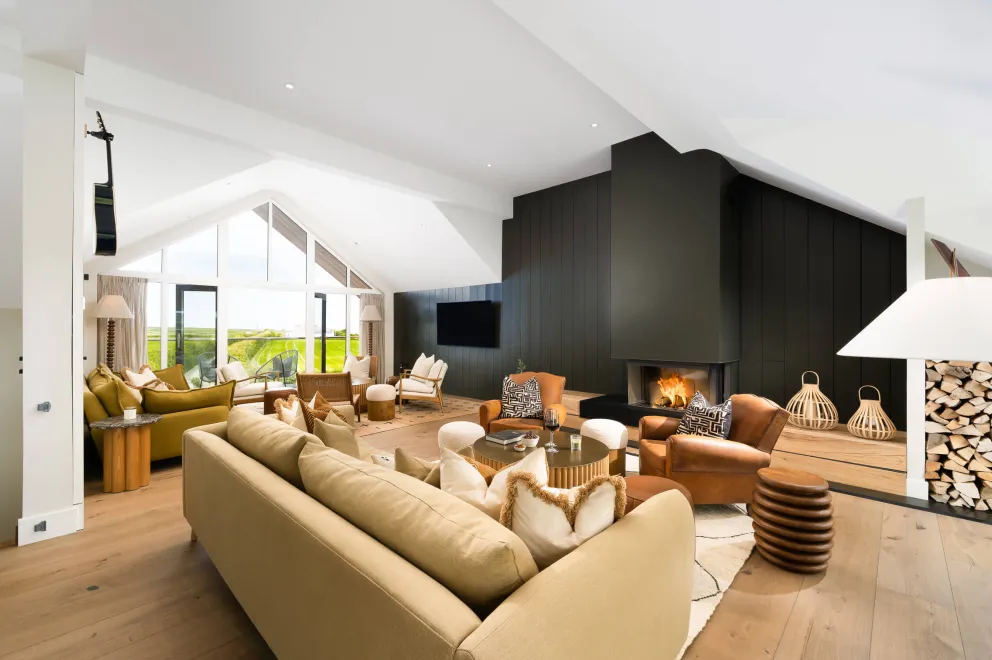 Living area with plenty of seating, a glass-fronted wood burner and green wooden panelling.