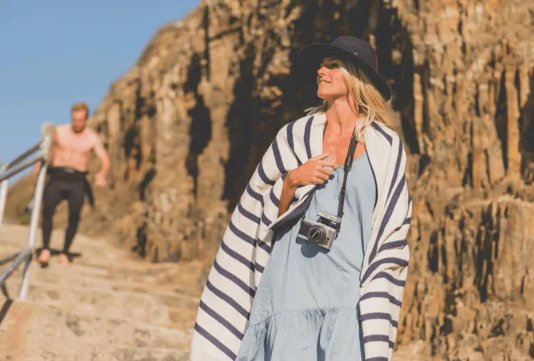 Woman walking to the beach wearing a striped top and a camera around her neck