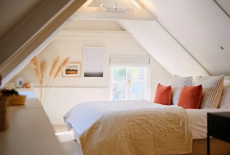 Master bedroom with low ceilings, art prints, pampas grass and orange cushions.