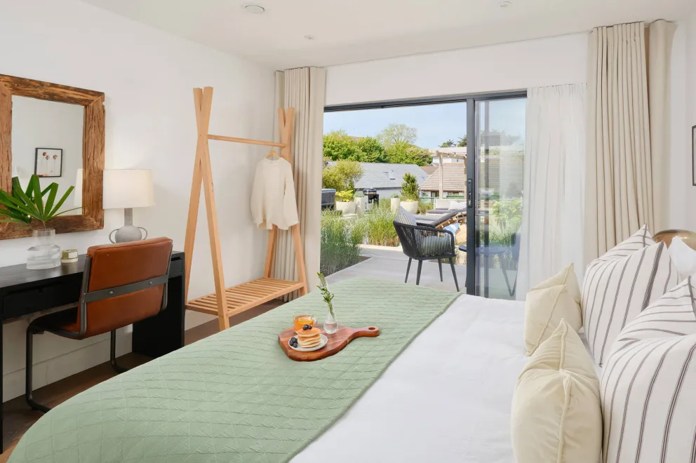 Bedroom with a bed and striped headboard, mint green bedspread and patio doors opening onto the garden.