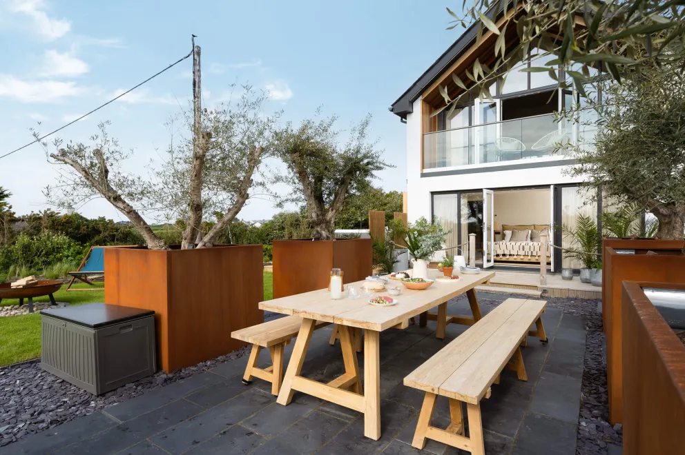 Outdoor patio with large wooden table laid with salad, plates and a vase of flowers.
