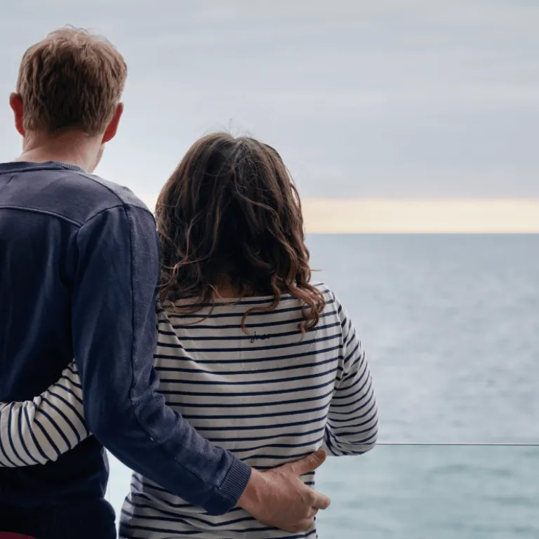 A couple admiring the view out to sea, with their arms around each other's back