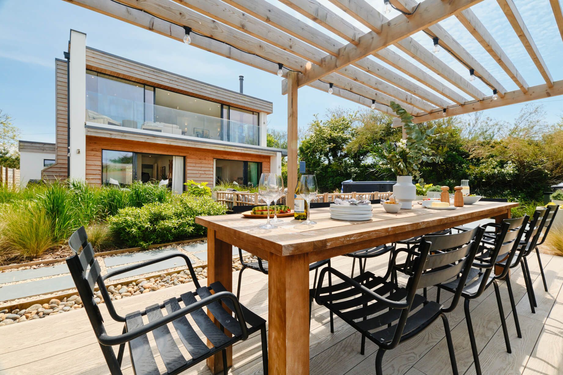 An outdoor table underneath a pergola, laid with a summer lunch spread.