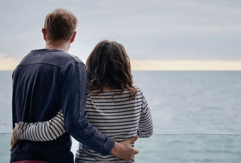 A couple admiring the view out to sea, with their arms around each other's back