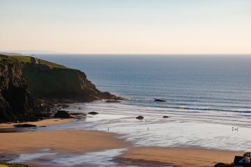 Mawgan Porth Beach in the early morning with surfers heading out.