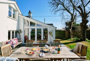 Outdoor table laid with lunch, in front of white fronted cottage and blue skies.