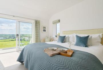 Four Geese's master bedroom, finished in green and blue touches with a large sliding door to the left and views over the countryside.