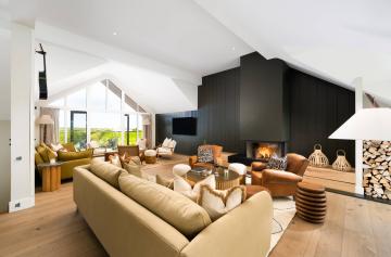 Living area with plenty of seating, a glass-fronted wood burner and green wooden panelling.