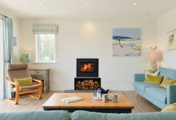 Four Geese's living room with a wood burner, arm chairs and large coffee table laid with a teapot and mugs.