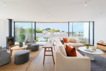 Living room with a wood burner to the left, two striped armchairs, wooden floors and a pale pink corner sofa.