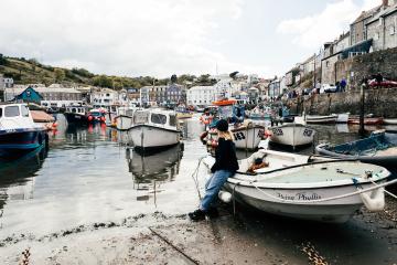 Girl leaning on moored boats in Mevagissey Harbour.