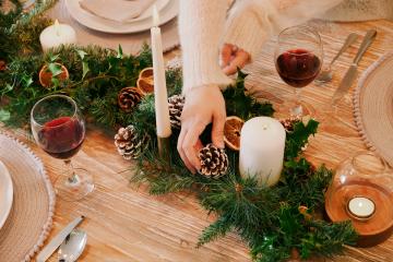Christmas table setting with red wine, and fir and holly centre piece.
