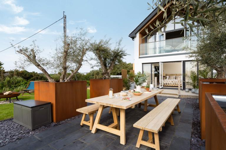 Outdoor patio with large wooden table laid with salad, plates and a vase of flowers.