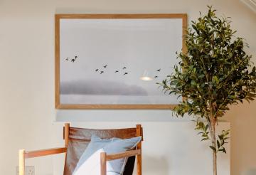 A low slung brown leather armchair with a potted tree and art print next to it.