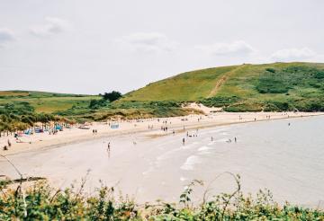 Sandy beach with grassy sand dunes and gentle waves.