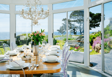 A conservatory set up for lunch, overlooking a large flower-filled garden