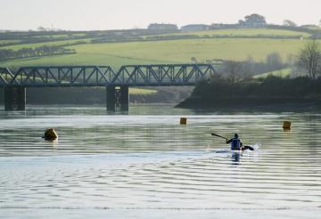 Kayaker paddling on calm waters in front of the Camel Estuary bridge.