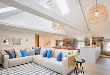 Large living room, with open-plan kitchen and dining room. Soft grey corner sofa with blue scatter cushions and striped rug.