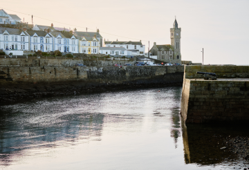 View over Porhleven Harbour, flanked by pretty coloured houses and with the clock tower in the distance.