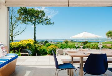 Ednovean House's dining room, with the large sliding doors open to reveal beautiful views over the coastline and St Michael's Mount in the distance.
