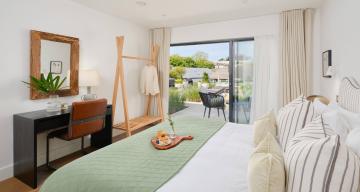 Bedroom with a bed and striped headboard, mint green bedspread and patio doors opening onto the garden.