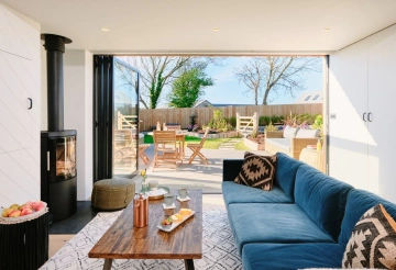 Scandi-inspired living room with blue sofa and wood burner, with the bifold doors open leading out onto the garden.