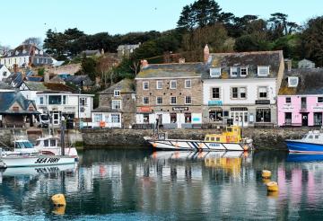 Padstow Harbour with boats on the water in the foreground and houses in the background.