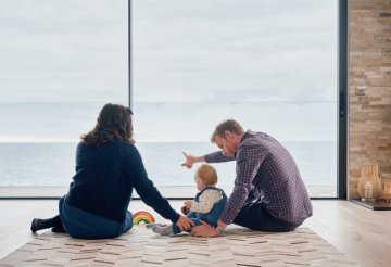 A mum and dad admiring the sea view from inside a house, with their daughter sitting between them