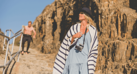 Woman walking to the beach wearing a striped top and a camera around her neck