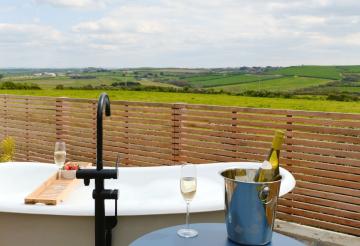 Outdoor bath with glasses of prosecco and views over the countryside.