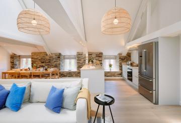 Large living room, with open-plan kitchen and dining room. Soft grey corner sofa with blue scatter cushions and striped rug.