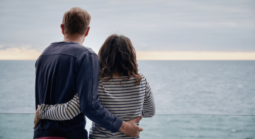 A couple admiring the view out to sea, with their arms around each other's back