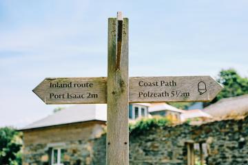 Wooden coast path sign post pointing towards Polzeath and Port Isaac.