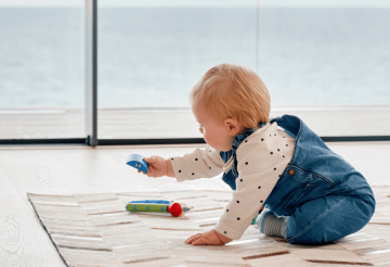 A toddler playing with wooden toys on a play mat, and the sea in the background
